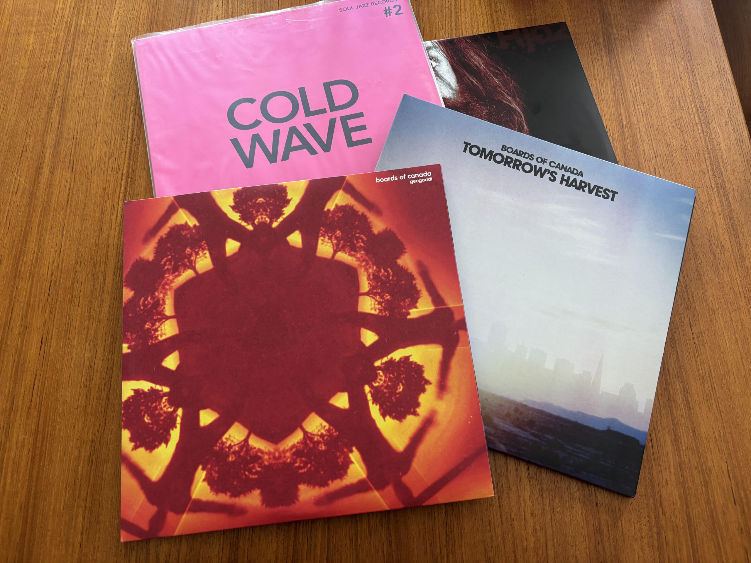 Stack of vinyl records featuring Boards of Canada and Cold Wave albums on a wooden table