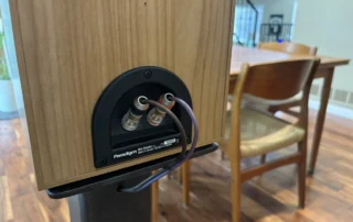 Back of a pair of bookshelf speakers with banana plug connections and properly gauged speaker wire attached to binding posts