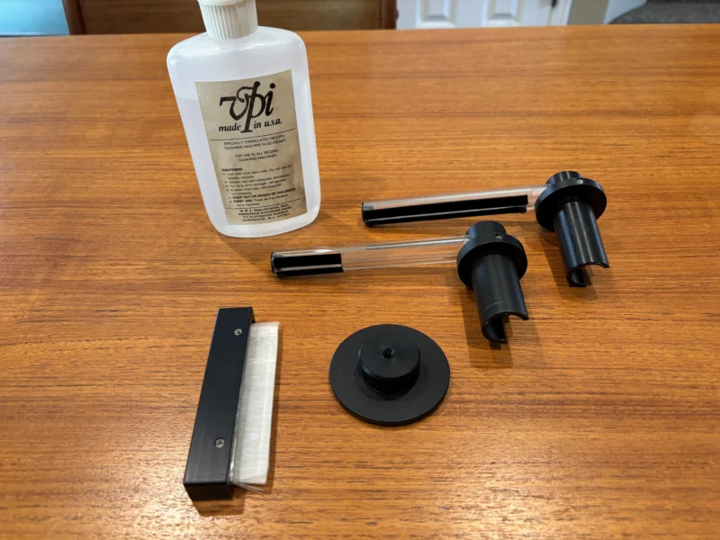 VPI HW-16.5 record cleaning machine accessories including cleaning fluid, record clamp, vacuum arm, and cleaning brush arranged for vinyl record maintenance