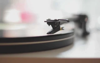 Turntable tonearm resting on a flat vinyl record with subtle center blur highlighting record weight or clamp effect on playback.
