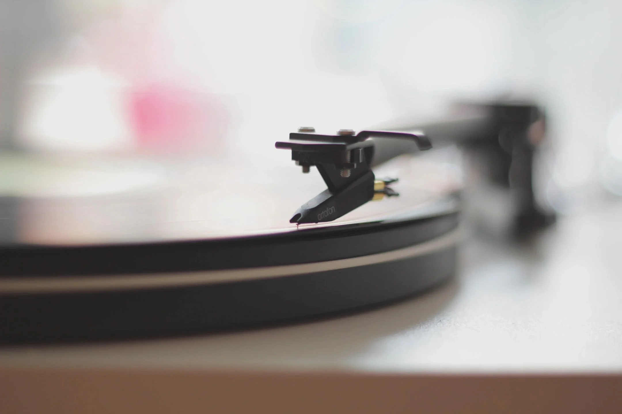 Turntable tonearm resting on a flat vinyl record with subtle center blur highlighting record weight or clamp effect on playback.