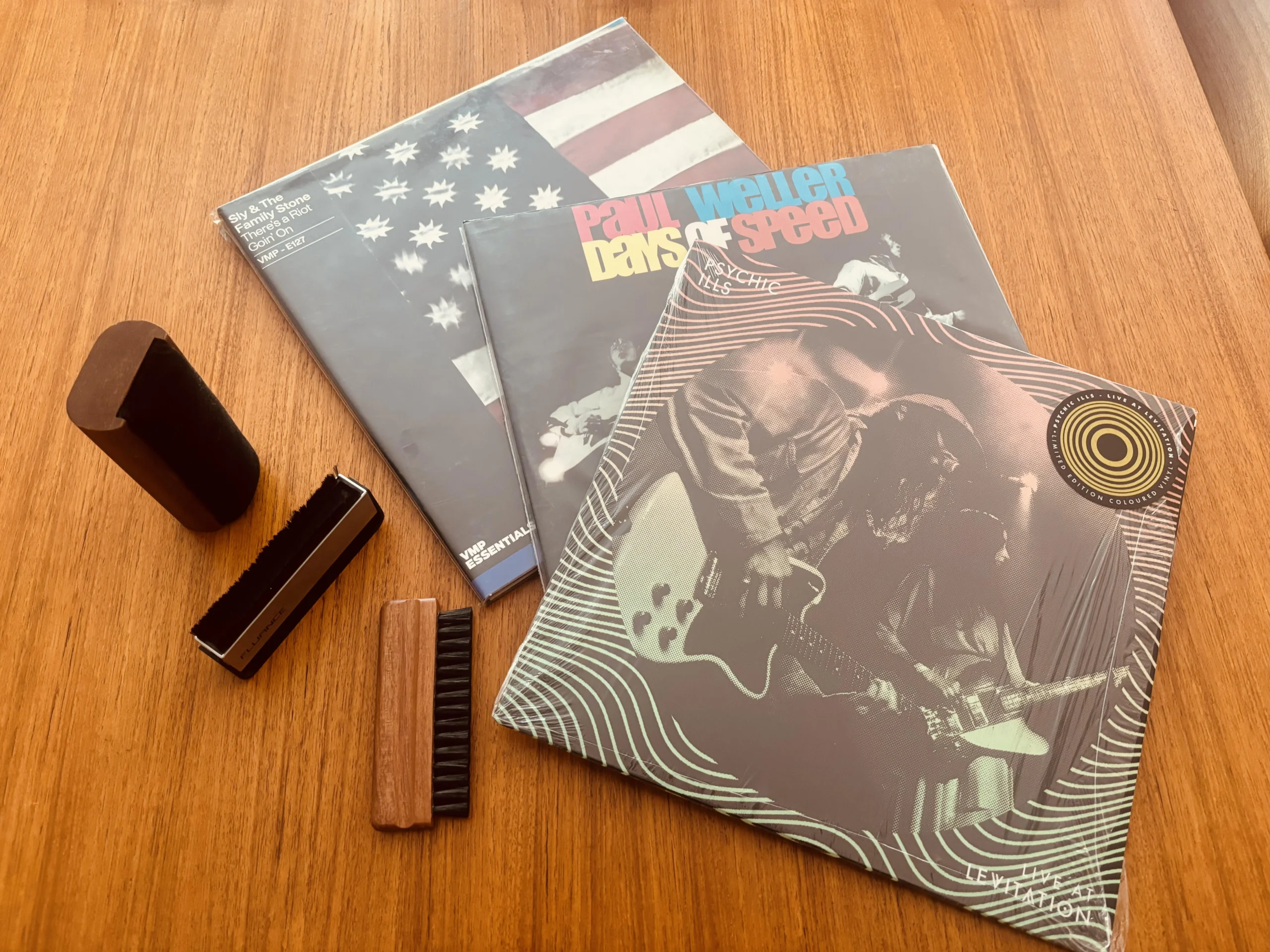 Three vinyl records with three different record cleaning brushes arranged on a table showing vinyl care tools and albums
