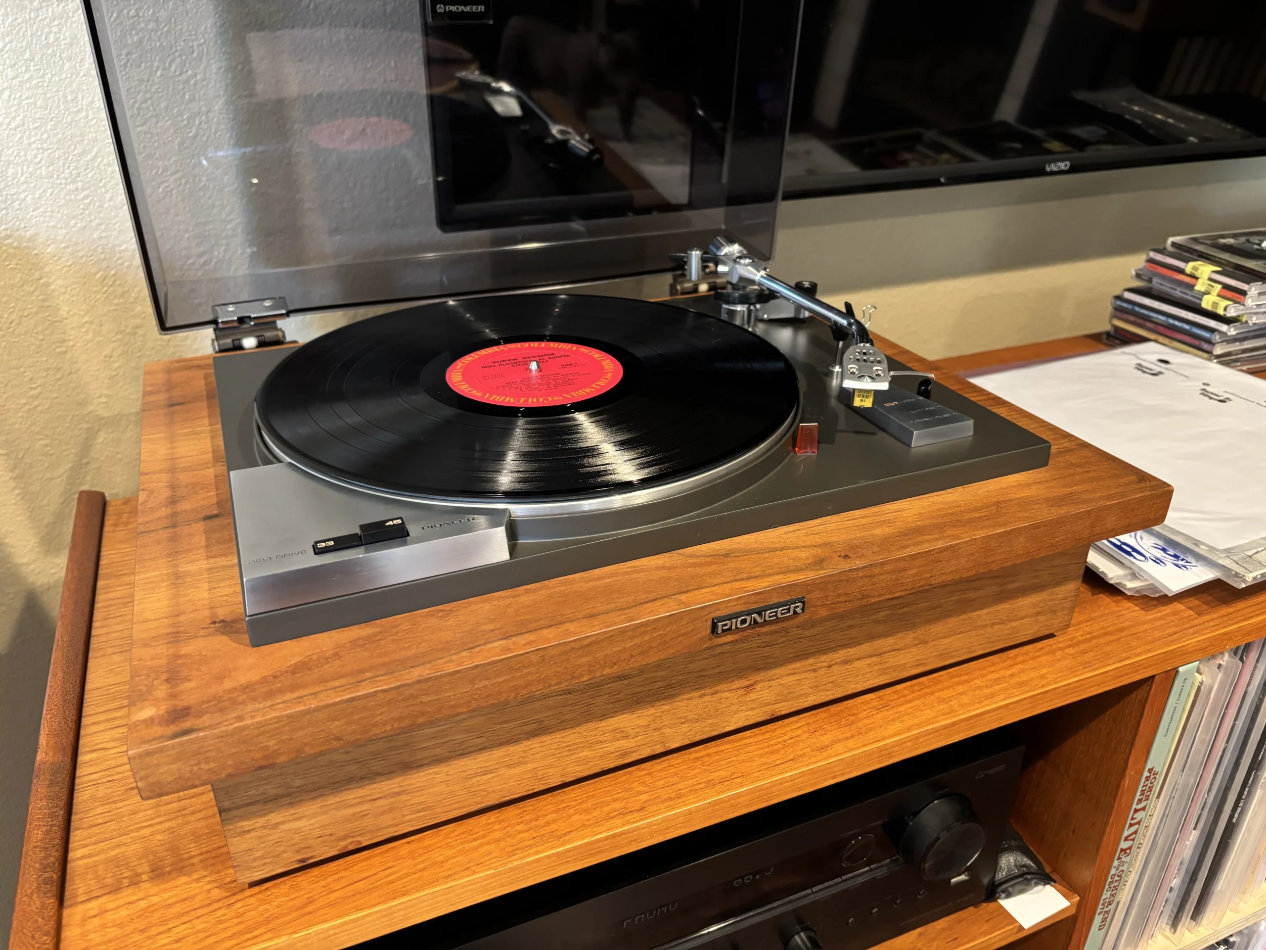 Pioneer PL-50 Turntable Ready to Play Vintage Pioneer PL-50 turntable with the dust cover open and a vinyl record on the platter, viewed from the front left, showcasing its walnut plinth and classic Japanese hi-fi design.